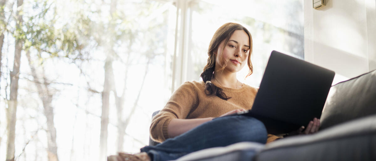 Frau sitzt mit Laptop auf dem Sofa © Mint Images / Getty Images