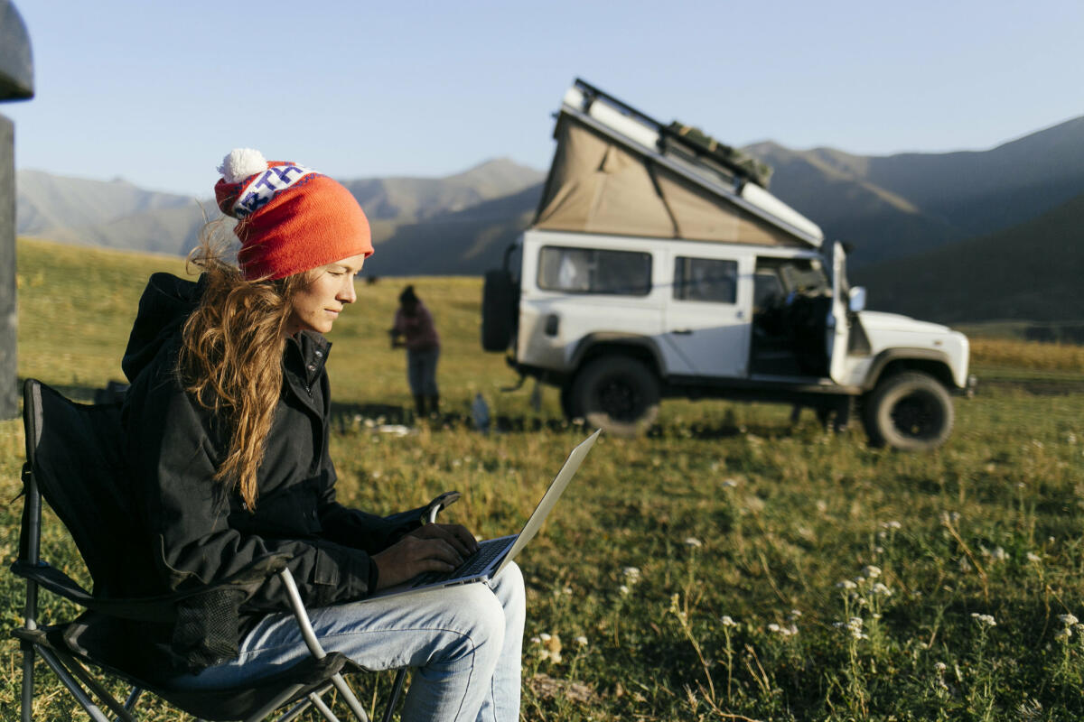 Frau sitzt vor einem Camper und arbeitet © Milo Zanecchia/ Ascent Media / Getty Images